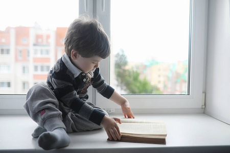 这个小男孩正在看书。那孩子坐在窗边