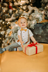 一个小男孩坐在一辆汽车的引擎盖上，圣诞树的背景是一个礼品盒