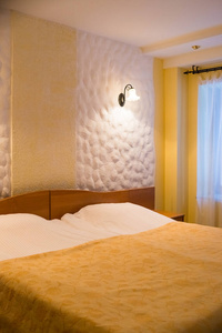 现代卧室等着新人。床上的黄色毯子在优雅的卧室内部。壁灯和灯具舒适家具.双人带双人床的浅色调酒店客房。