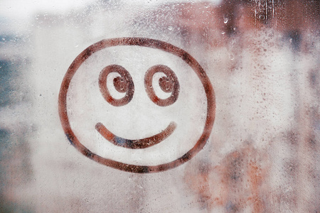 在城市模糊的玻璃背景上,画在满是雨滴的窗户上的幸福笑脸照片