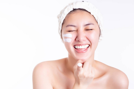 年轻女子展示面霜,润肤霜在脸上,手指上.微笑的亚洲美女得到幸福.