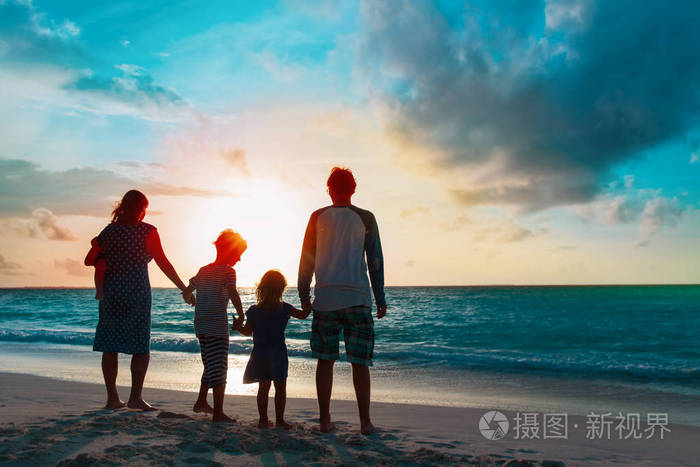 快乐的一家人带着树孩子在日落海滩散步
