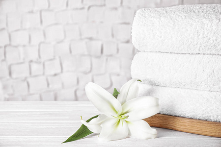 Stack of clean bath towels and beautiful flower on white wooden 