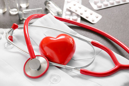 听诊器，医生制服，心脏和药片，灰色背景。心脏病学概念