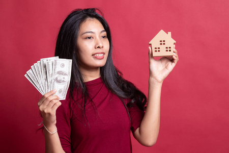 钱和孤立的房子快乐的年轻亚洲女人,有房子模型和一堆钱银行照片