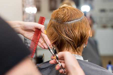女发型师在发廊用剪刀剪头发.理发师用手指夹住发夹,梳子和剪刀特写.