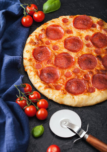 新鲜的圆形烤意大利辣香肠比萨和黑色背景的罗勒西红柿。俯视图