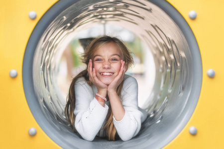 Pretty, little girl, having fun, lying on pipe on children playg