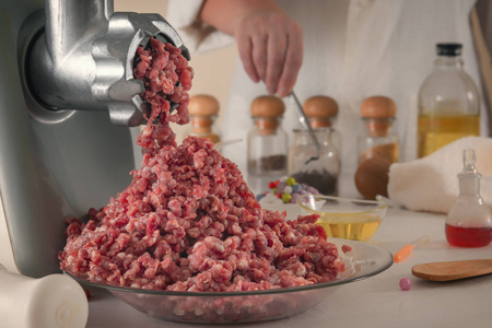 碎肉从绞肉机里出来，背景是一个化学实验室的玻璃器皿。人造肉的制造。特写