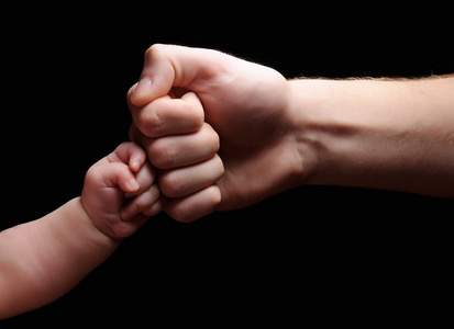 孩子和父亲的手。拳头在一起。黑色背景