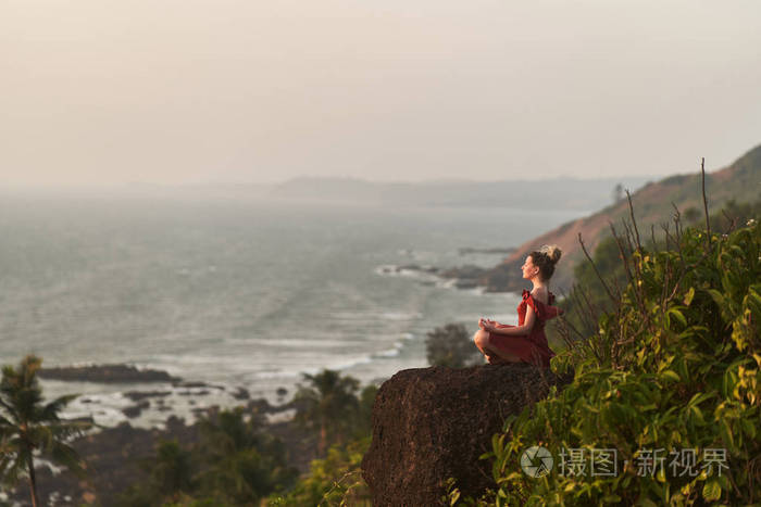 在印度的一座山上，一个年轻女孩穿着红裙子练习瑜伽