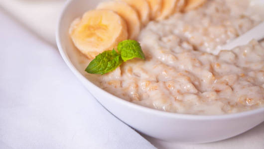 白桌上的白碗里放着香蕉燕麦粥。健康早餐。闭合。