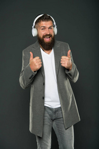对科技竖起大拇指。快乐的时髦人士戴上无线耳机。胡子男人喜欢听音乐。立体声技术。新技术。商务和娱乐科技