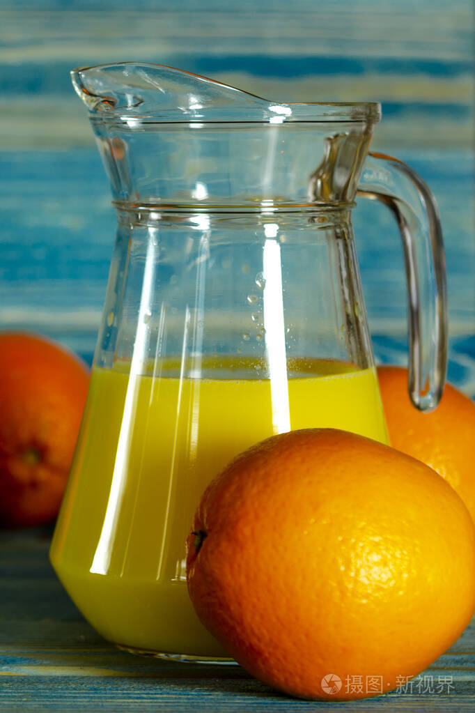 绿色背景的木制桌子上的玻璃杯和橙汁罐