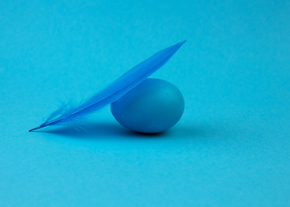 复活节蓝色背景的单色彩蛋和羽毛。复活节快乐贺卡。最小复活节概念。