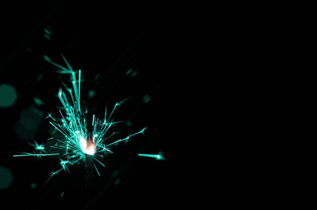 Sparkler in turquoise and white light on a black background. 