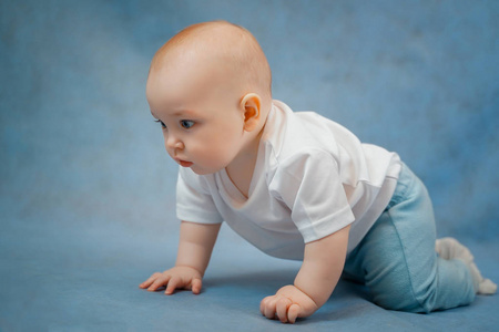 Cute little baby in light clothes crawls on all fours on a blue 