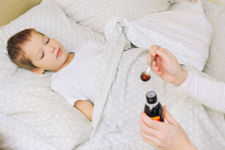 一个金发男孩病了,躺在床上,用勺子给他喝药水照片