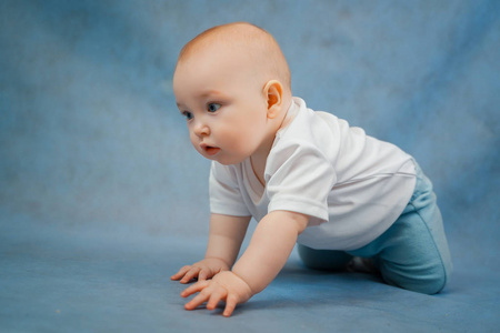 Cute little baby in light clothes crawls on all fours on a blue 