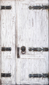 破旧的白色木门，有锻造的铰链和狮子头环形状的把手