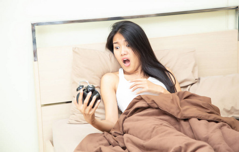 早上被惊醒的睡过头的女人和闹钟坐在床上昏昏欲睡的小女孩正在睡觉