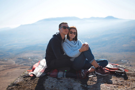 A loving couple with a backpack sits on a rock in the mountains 