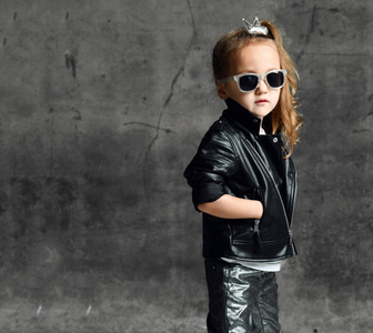 女孩穿着皮夹克,牛仔裤,戴着墨镜,在水泥墙上摆出一副骑自行车的摇滚