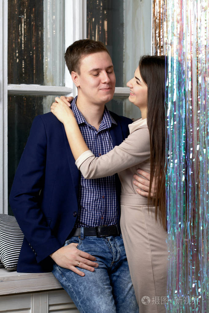 一个年轻人拥抱他的妻子.她抱住他的脖子.靠近闪亮的雨幕.