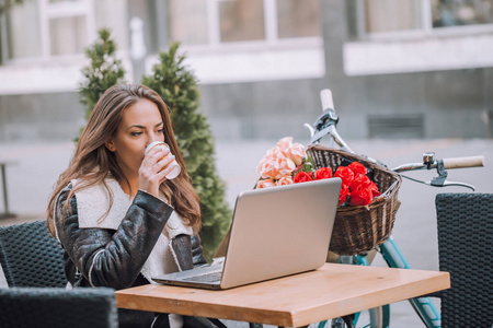 年轻女子在街边咖啡厅用笔记本电脑喝咖啡
