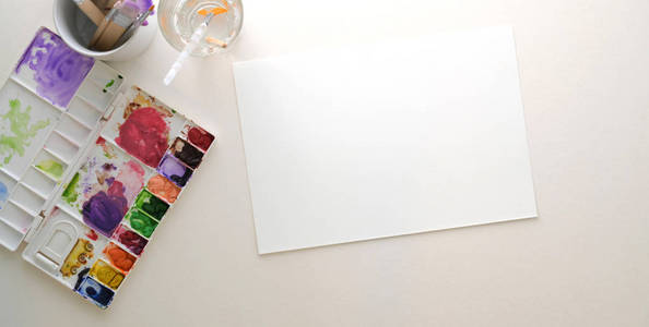 在白色桌子背景上，用素描纸和绘画工具拍摄的现代艺术家工作场所的俯视照片