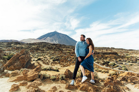 一对美丽的年轻情侣在火山背景下的岩石地上摆姿势