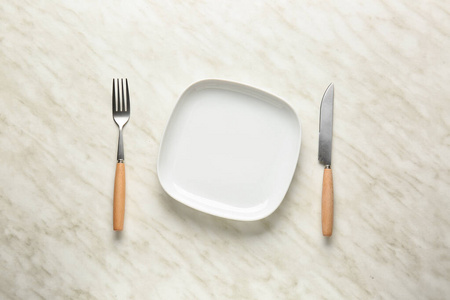 Empty plate and cutlery on light background