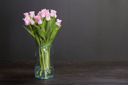 深色木桌上有粉红色郁金香的玻璃花瓶，背景或概念