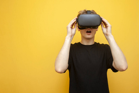 惊讶的年轻人带着VR眼镜在黄色背景下看着恐怖和尖叫，男人使用虚拟现实眼镜和恐惧