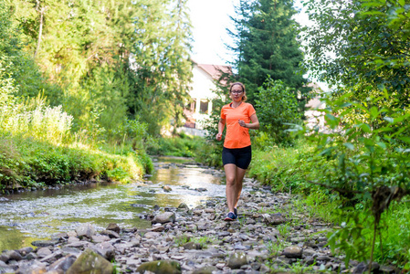 穿着鲜橙色T恤的女孩沿着山河奔跑。