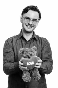 摄影棚拍摄正式的年轻快乐男子微笑着抱着泰迪熊，心和爱的标志