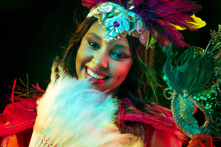 美丽的年轻女子在狂欢节面具和化装服装在五颜六色的灯光下
