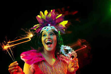 美丽的年轻女子在狂欢节面具和化装服装在五颜六色的灯光下