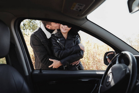 一对快乐的旅行情侣穿着黑色时尚的衣服，在田野路上享受汽车旅行，度假的概念
