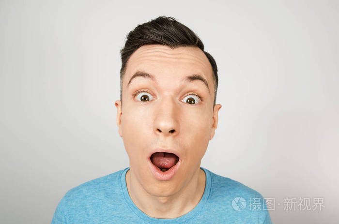 年轻人惊讶地张大了嘴穿着浅背景的蓝色t恤衫