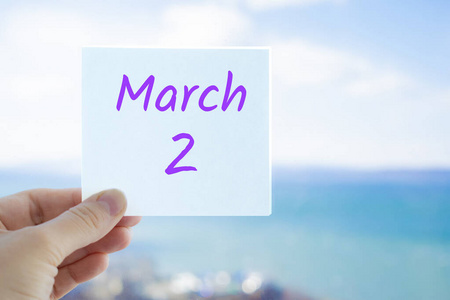 3月2日。3月2日，在模糊的海天背景上，手持贴纸。复制文本空间。日历概念中的春月