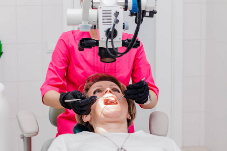 一位女性专业牙医在她的办公室里用雄蕊显微镜检查一位女性病人。雄蕊学家职业概念