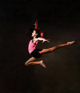 年轻苗条的运动女孩体操舞蹈演员跳起来，手臂伸直，在演播室做体操练习
