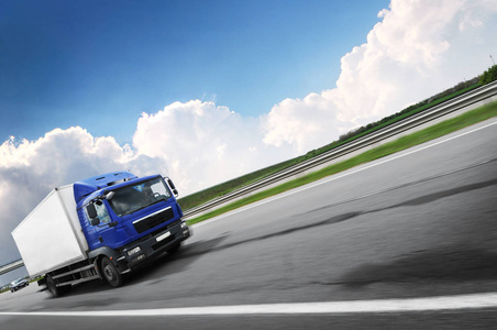 A truck driving fast on the countryside road against a sky with 