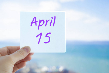 4月15日。4月15日，在模糊的海天背景上，手持贴纸。复制文本空间。日历概念中的春月