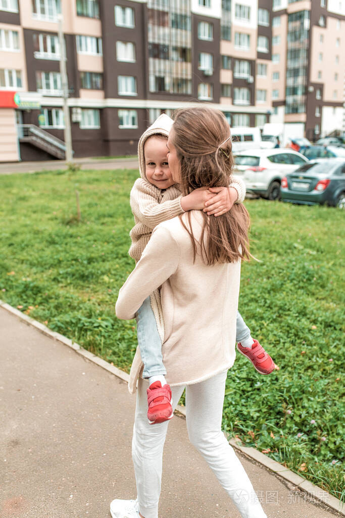 女人妈妈抱着男孩的孩子夏天在秋天的下午在城里散步穿着休闲的衣服