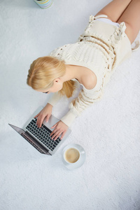 年轻女子躺在地毯上，手里拿着笔记本电脑