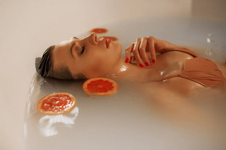 性感的年轻女人，皮肤完美，沐浴在牛奶和葡萄柚圈里
