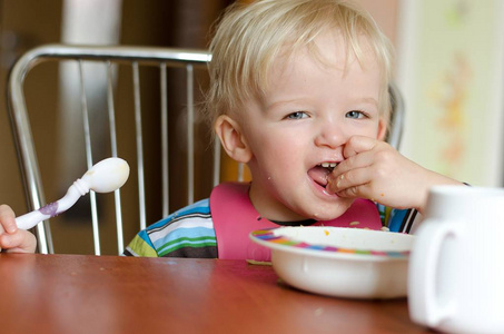 Happy blond boy sitting at the big table and chair as an adult. 