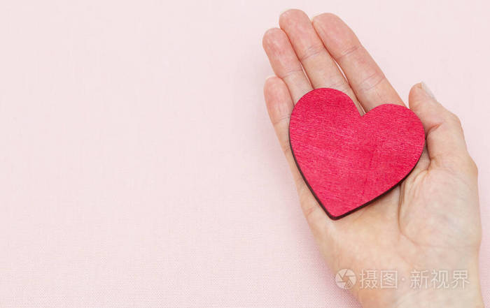 一个男人在粉红色的背景上手掌里握着一颗红色的心